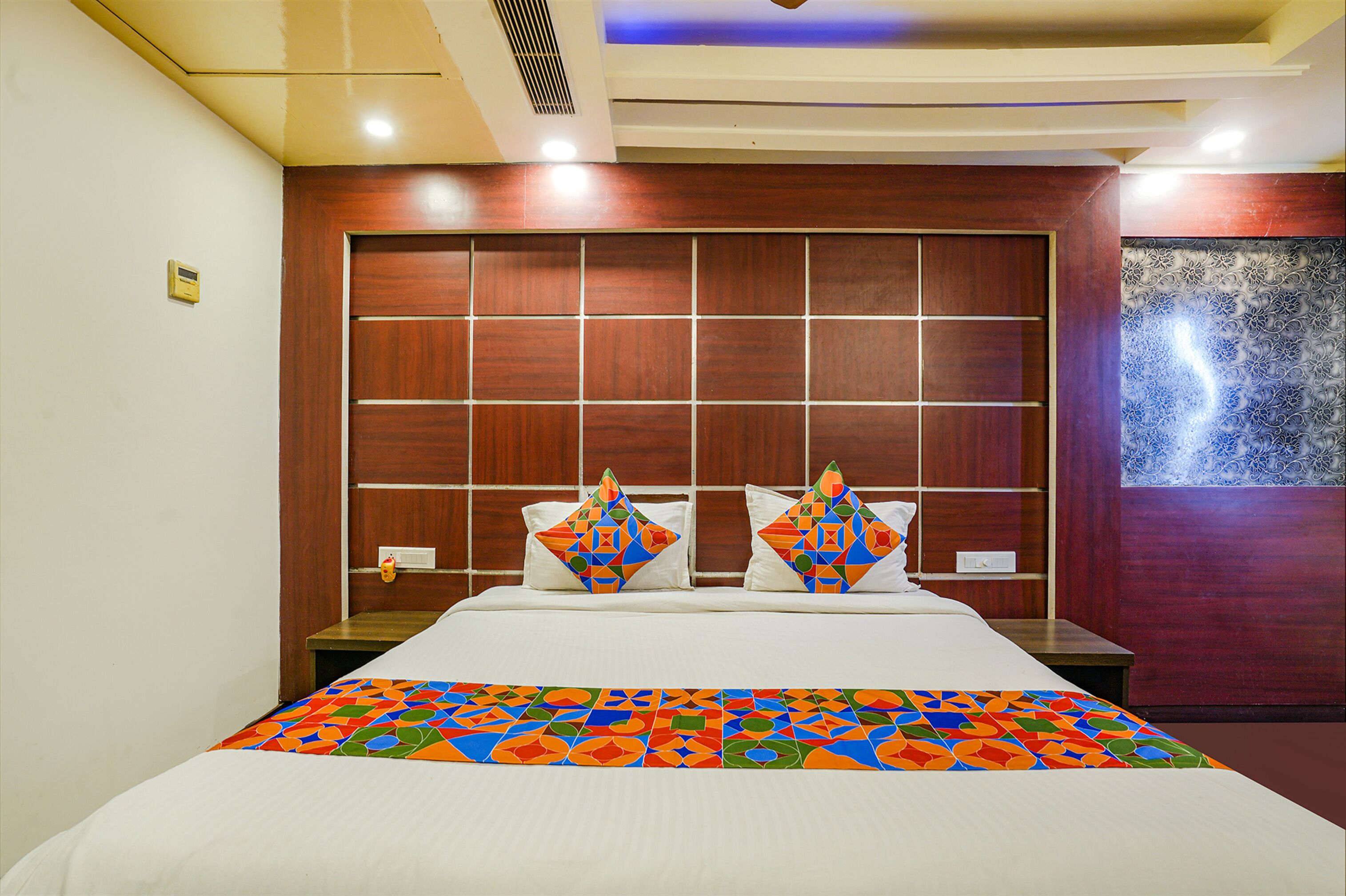 A hotel room with a large bed, wooden headboard, and a colorful bedspread.