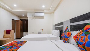 Quarto de hotel com duas camas, uma cadeira, aparelho de ar condicionado e janela com cortinas.