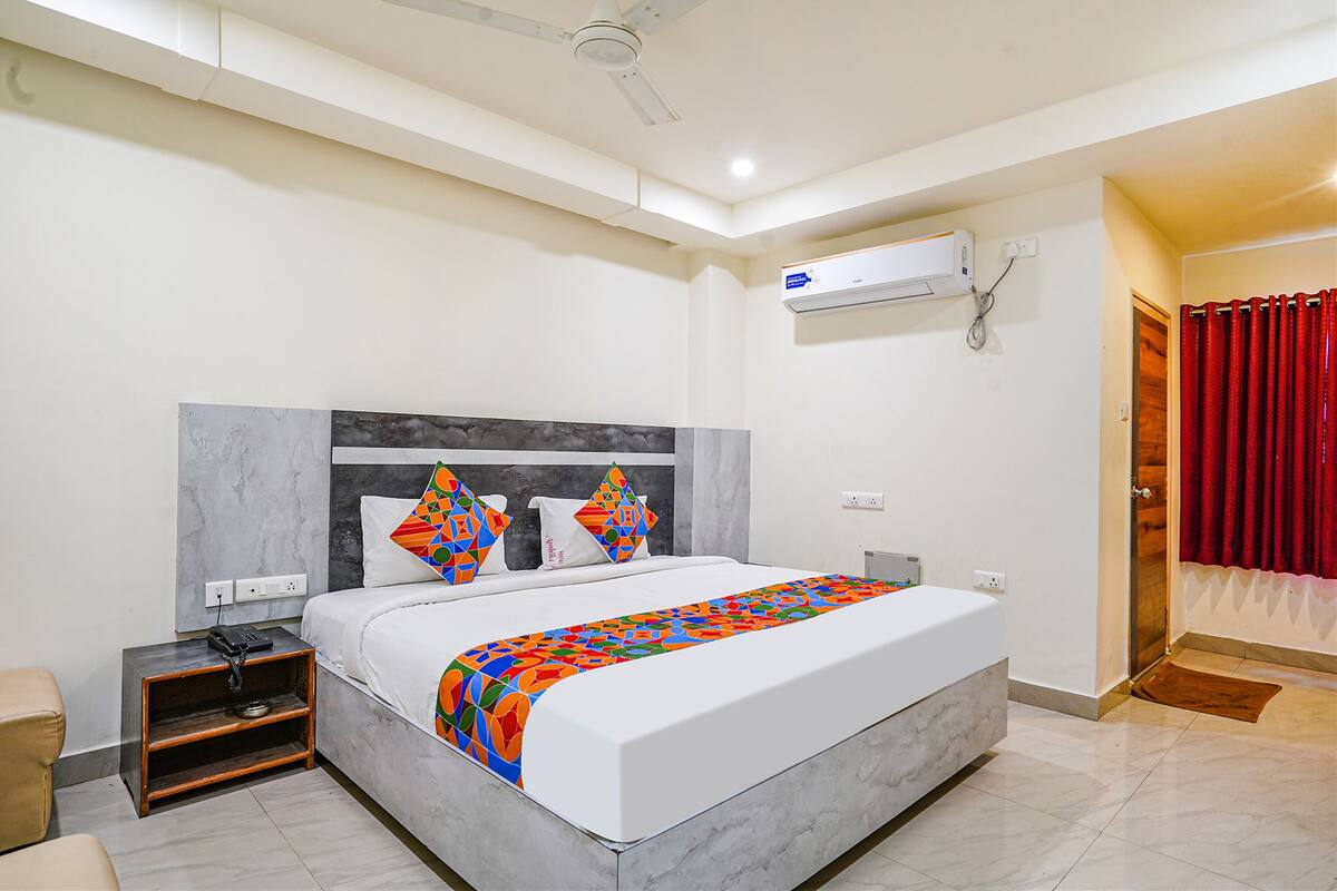 Camera d'albergo moderna con un letto grande, un comodino, un tavolo di fianco al letto e un condizionatore d'aria, con una tenda rossa.