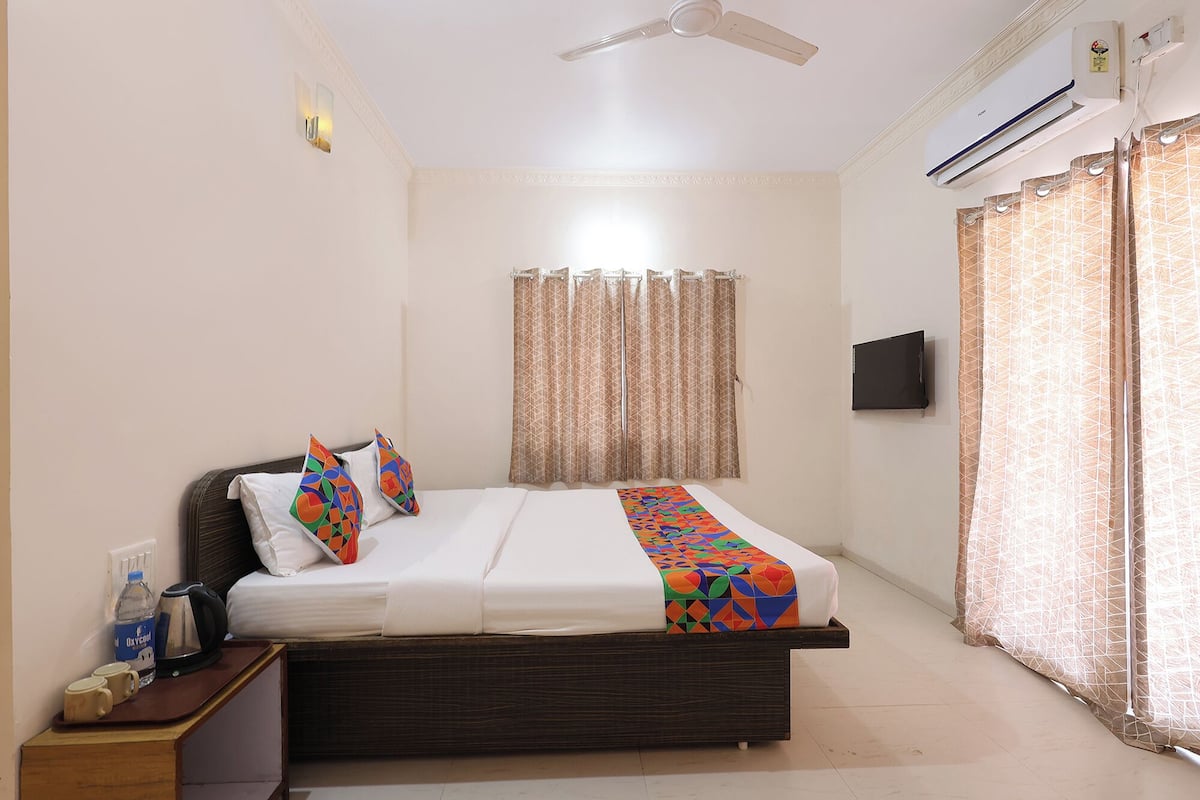 A neatly arranged bedroom with a bed, a bedside table with a kettle, a water bottle, and a mug.