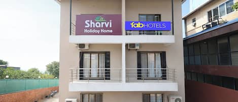 A building with a sign for 'Sharvi Holiday Home' and 'Tab Hotels'. It has a flat roof, multiple windows, and air conditioning units.