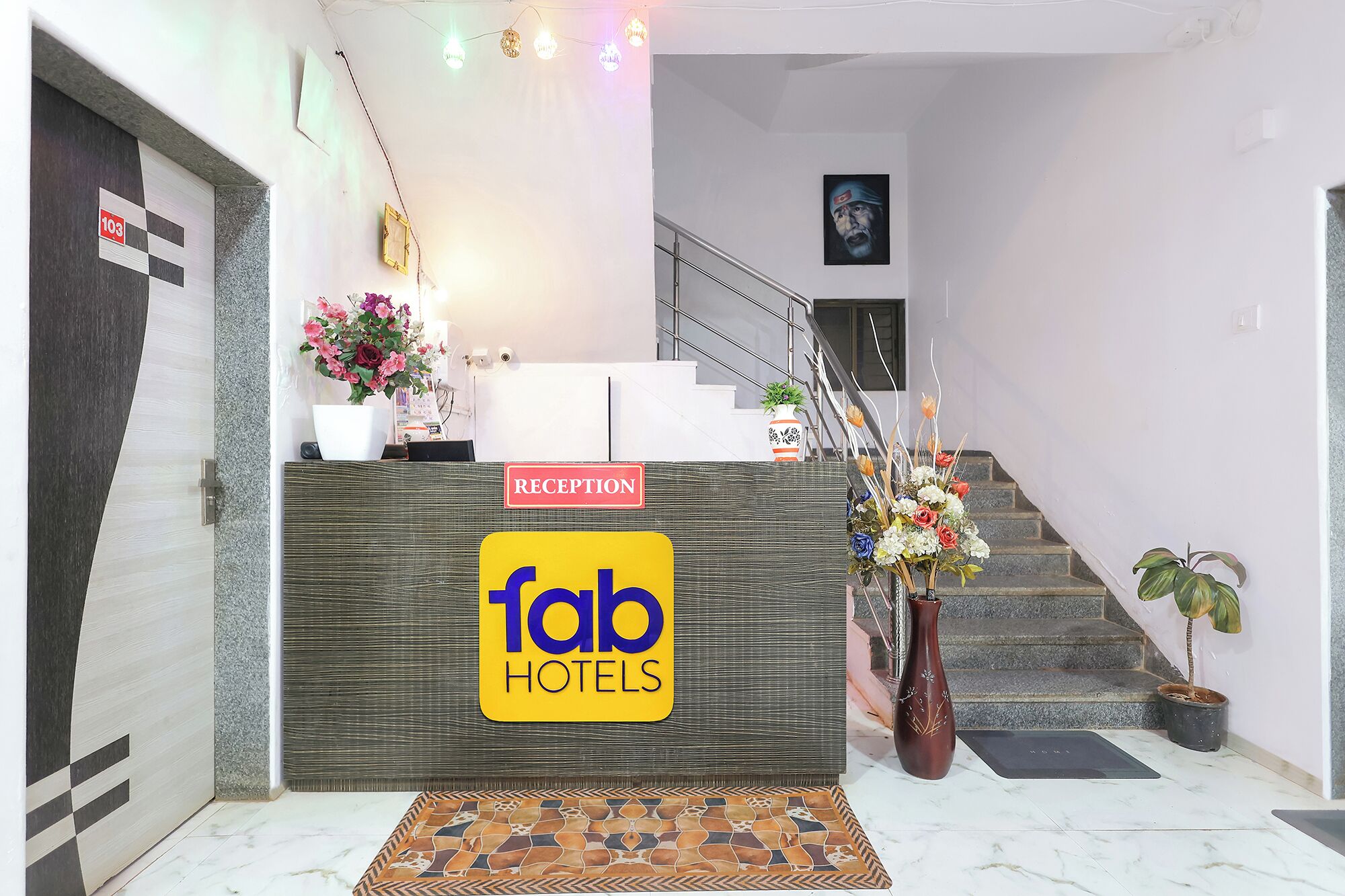 A reception area with a 'Tab Hotels' sign, a reception desk, a staircase, and a floral arrangement.