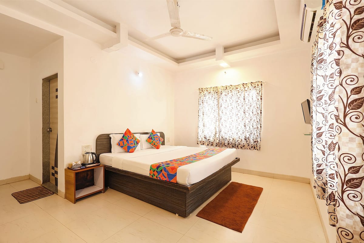 A bedroom with a bed, a bedside table, a ceiling fan, a window with patterned curtains, and a door.