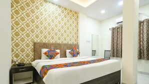 Une chambre moderne avec un papier peint à motifs, un lit agrémenté de coussins colorés, une table de chevet avec un téléphone, et une salle de bain avec un rideau de douche.