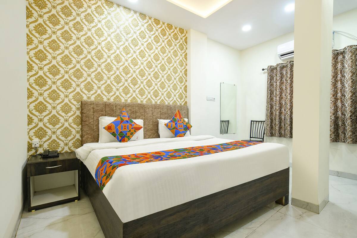 A modern bedroom with a patterned wallpaper, a bed with colorful pillows, a bedside table with a phone, and a bathroom with a shower curtain.