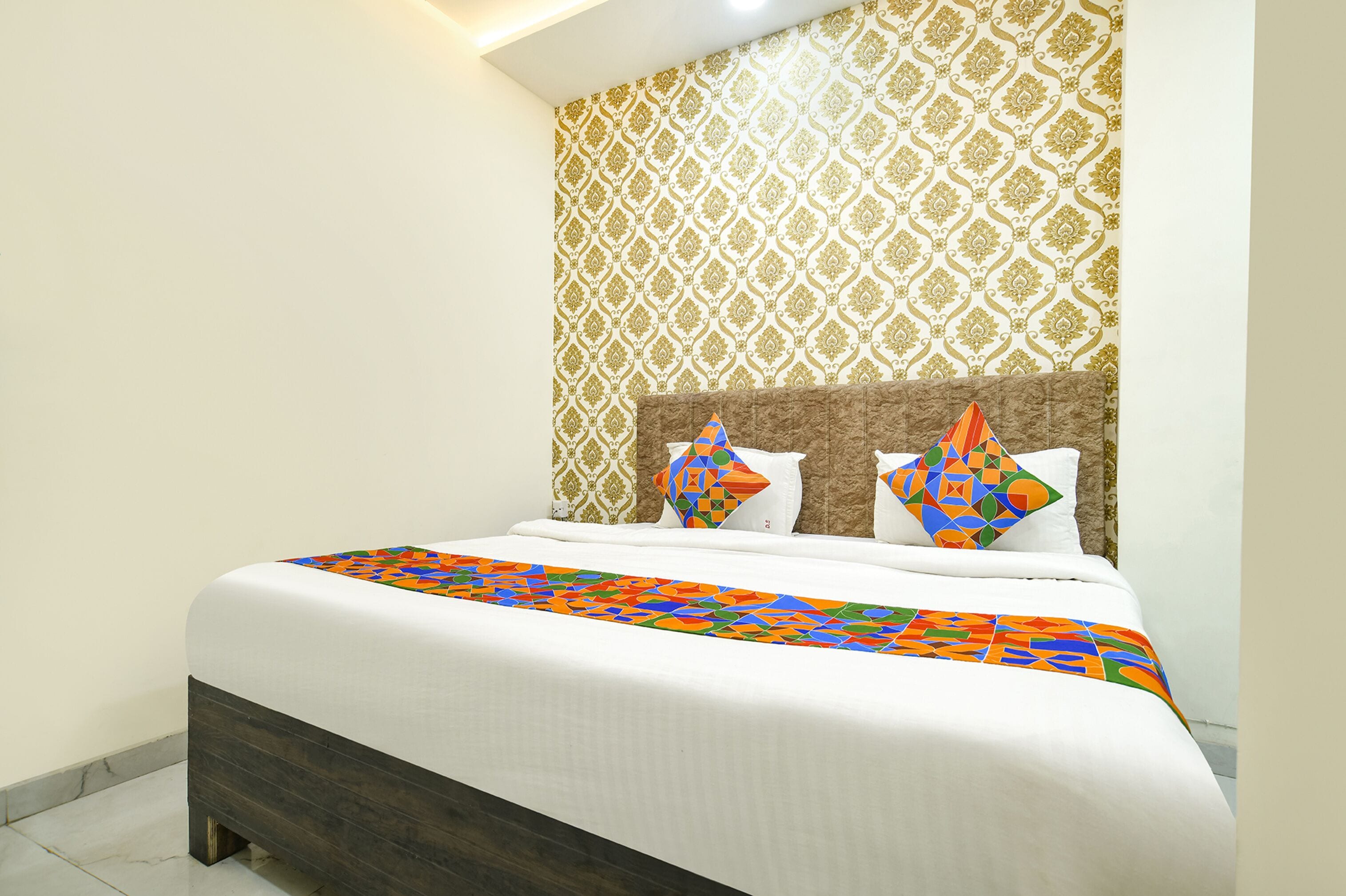 A neatly made bed with a patterned bedspread, a headboard with decorative pillows, and a patterned wallpaper on the wall.