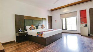 A modern hotel room with a large bed, a wooden headboard, a nightstand, a ceiling fan, and a window with a view. - Fabhotel Paradise Ville Resort (Nainital)