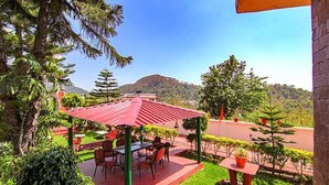 An outdoor patio with a red roof, surrounded by greenery and a view of hills. - Fabhotel Paradise Ville Resort (Nainital)