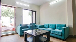 A living room with a blue sofa set, a coffee table, and a large window providing natural light. - Fabhotel Paradise Ville Resort (Nainital)