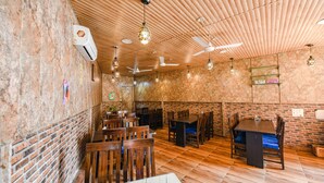 Interior de un restaurante con paredes de ladrillo, techo de madera, varias mesas y sillas, y ventiladores de techo.