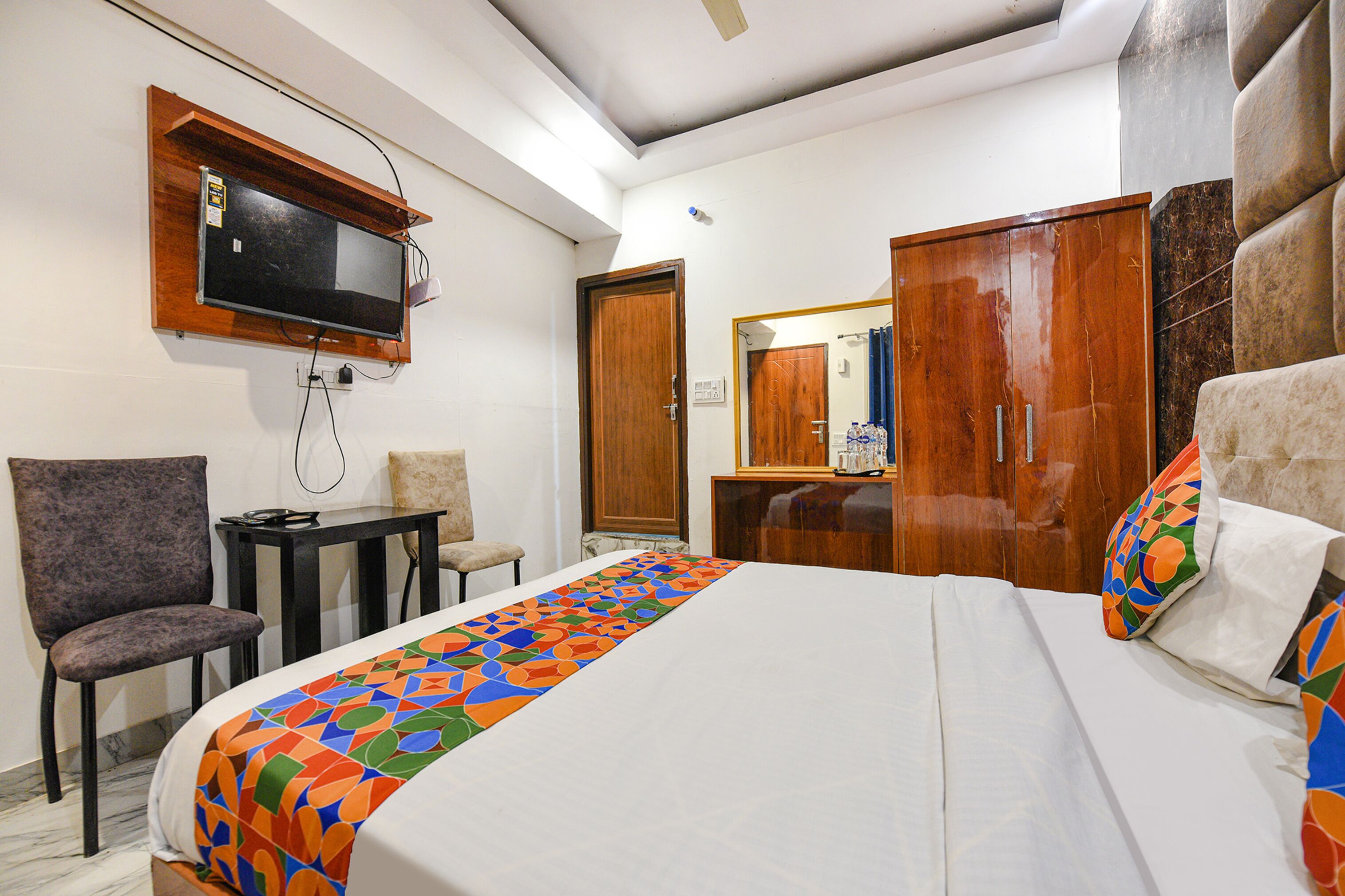Una habitación de hotel con una cama, televisión montada en la pared, un escritorio y una silla.