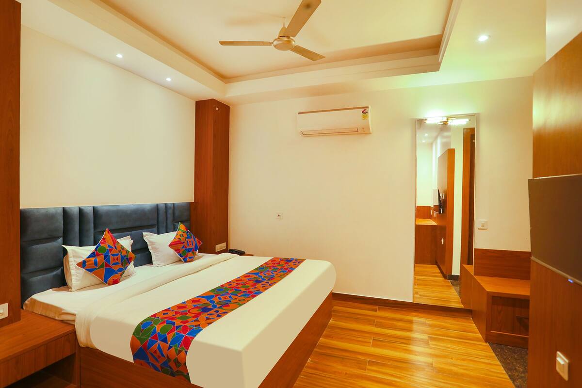 A modern hotel room with a large bed, a ceiling fan, an air conditioning unit, wooden flooring, and a wooden headboard.