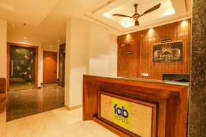 A hotel reception area with a wooden reception desk, a ceiling fan, and a reception sign. - Fabhotel Prime Swarn Bhoomi (Kanpur)