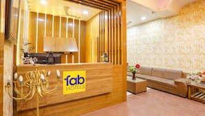 A hotel reception area with a wooden reception desk, a sofa, and a patterned wall. - Fabhotel Uday Villa (Kanpur)