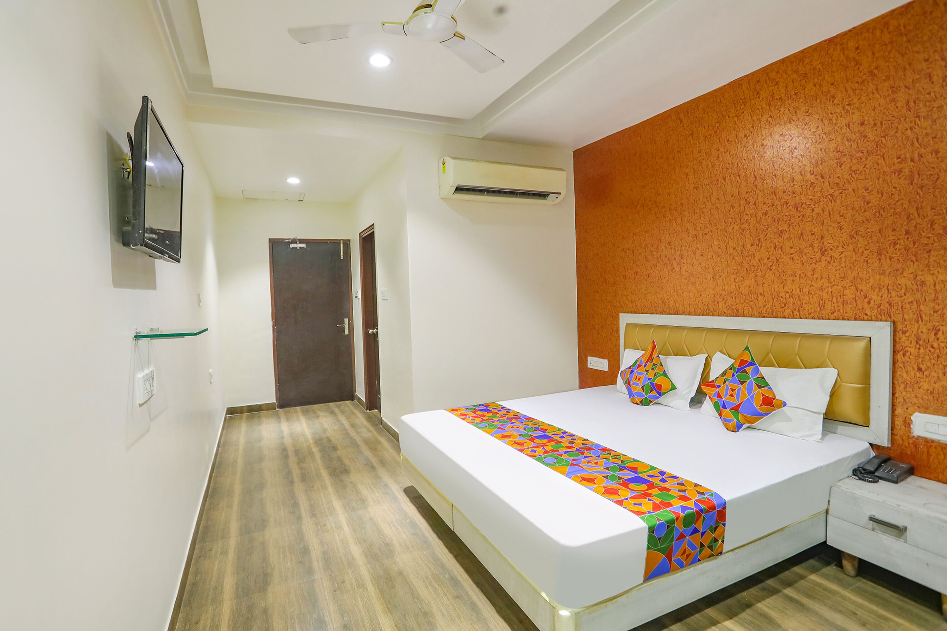 A hotel room with a bed, a bedside table, a telephone, and an air conditioning unit.