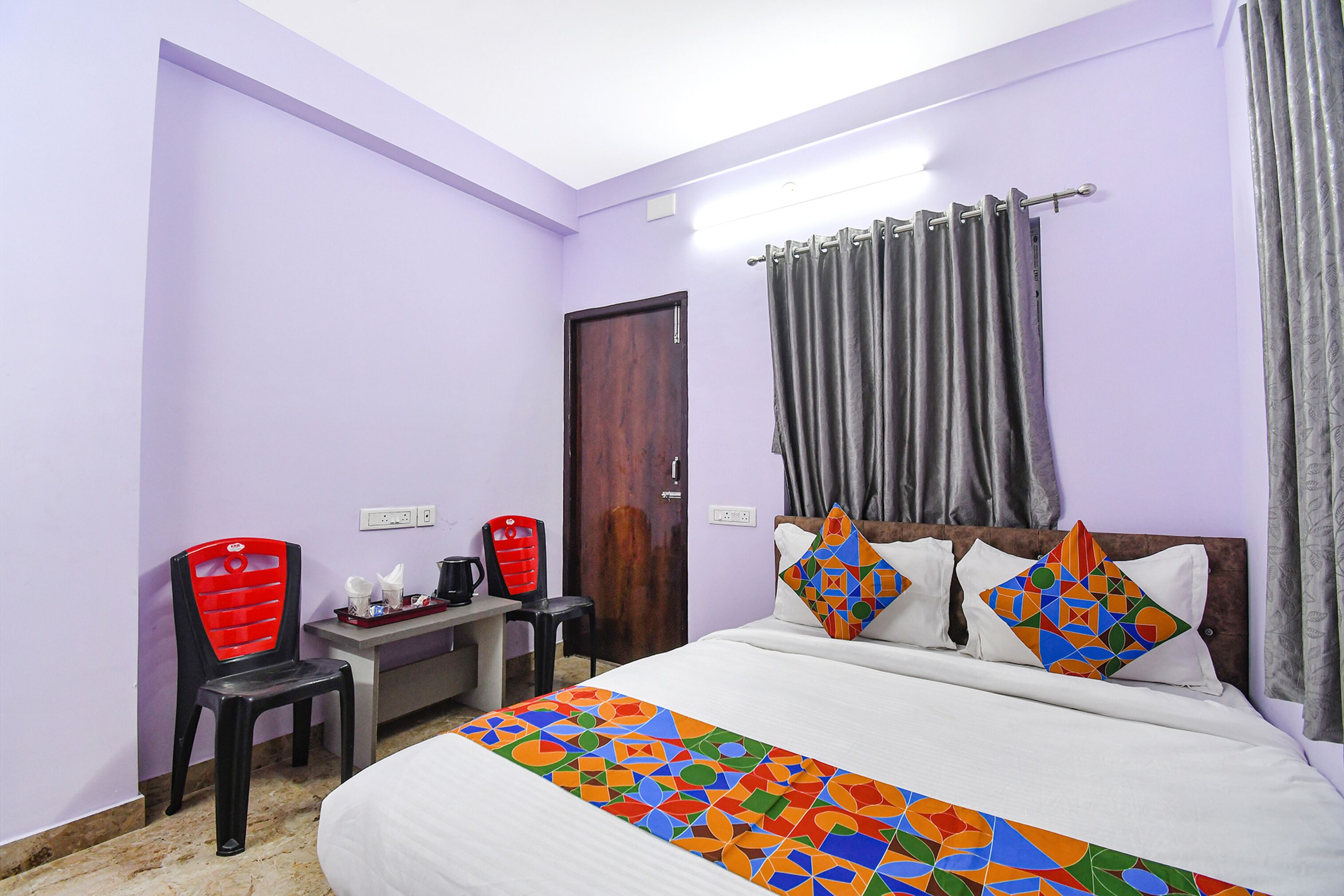 A hotel room with a bed, a desk, a chair, and a door.
