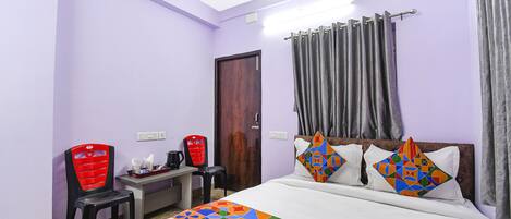 A hotel room with a bed, a desk, a chair, and a door.