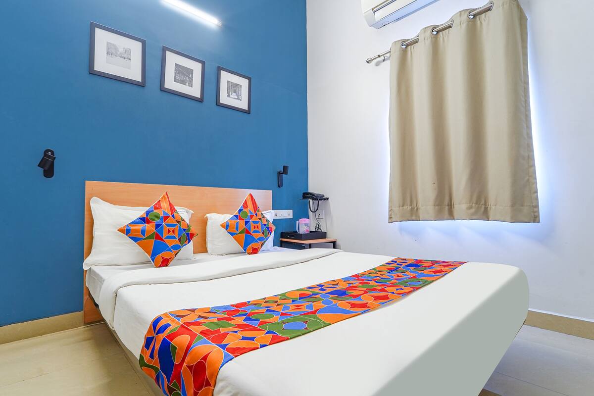 A hotel room with a bed, two pillows, a nightstand, a lamp, and a window with curtains.