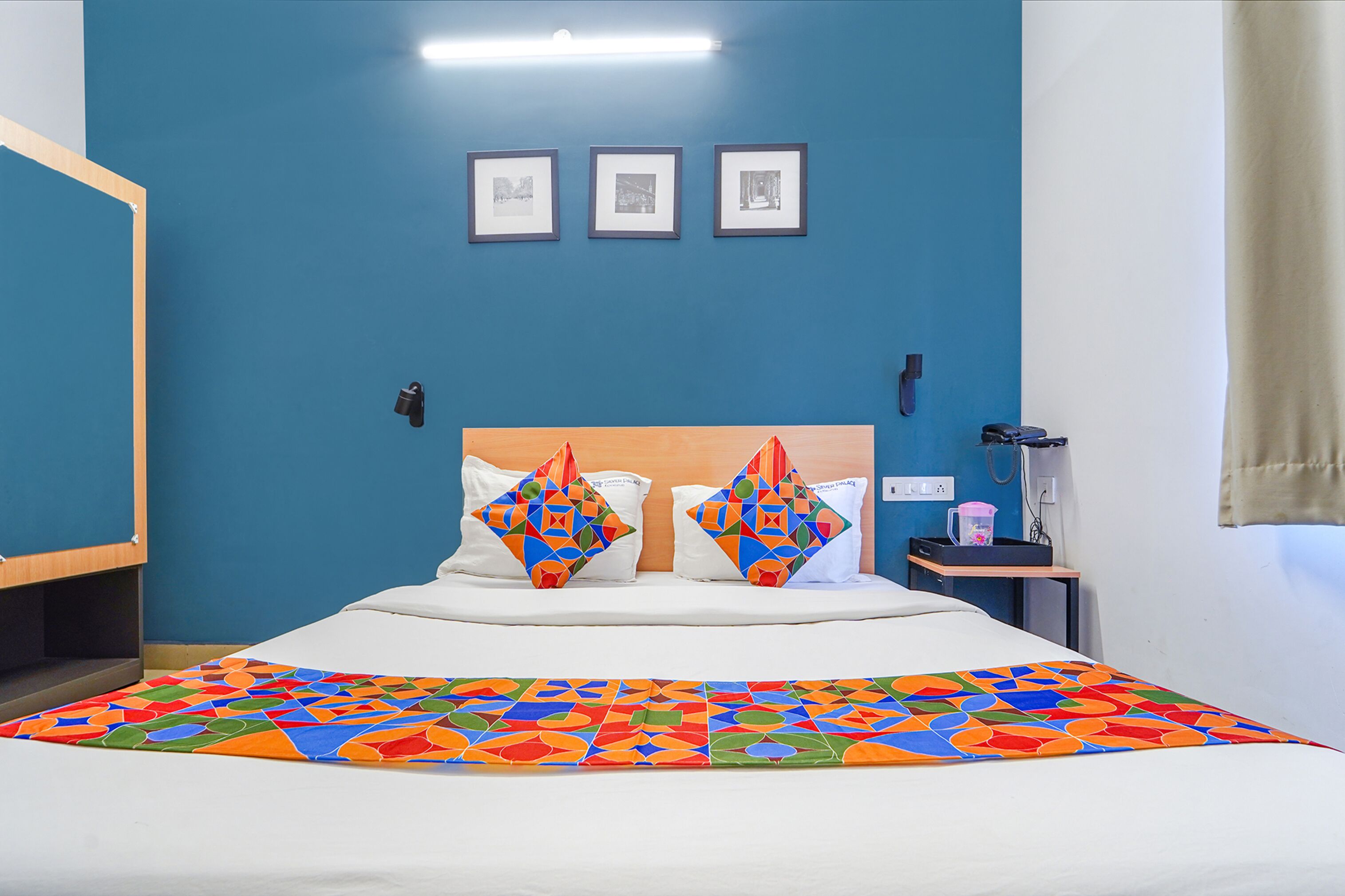 A hotel room with a bed, a nightstand, a lamp, and a wall with three framed pictures.