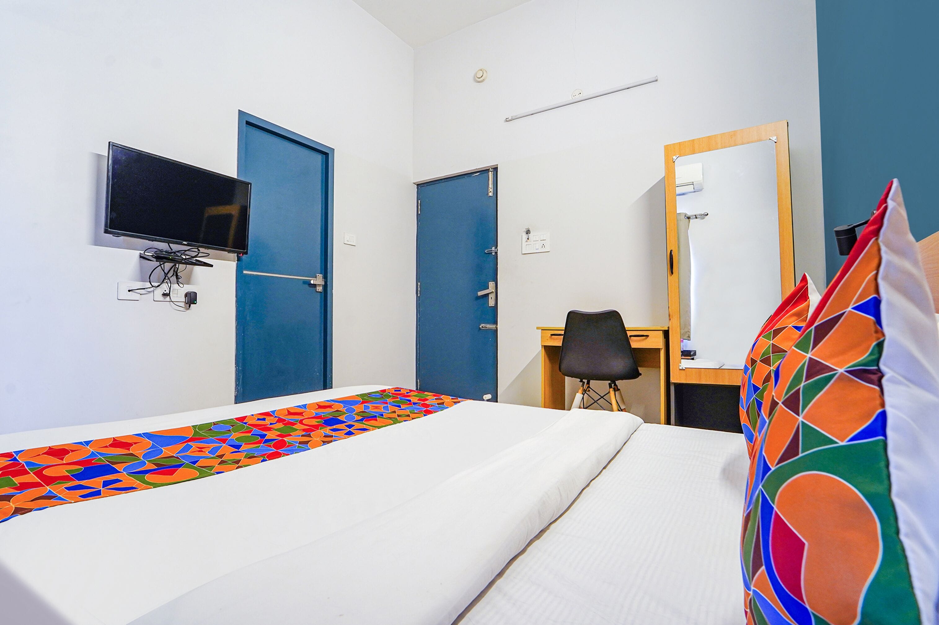 A hotel room with a bed, a desk, a chair, a television, and two doors.