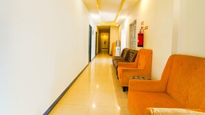 A hotel lobby with a long corridor, orange seating area, and a fire extinguisher on the wall. - Fabexpress Silver Palace (Chennai)