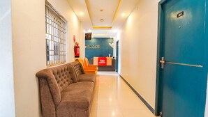 A hotel lobby with a reception desk, a blue door, a brown sofa, and a fire extinguisher. - Fabexpress Silver Palace (Chennai)