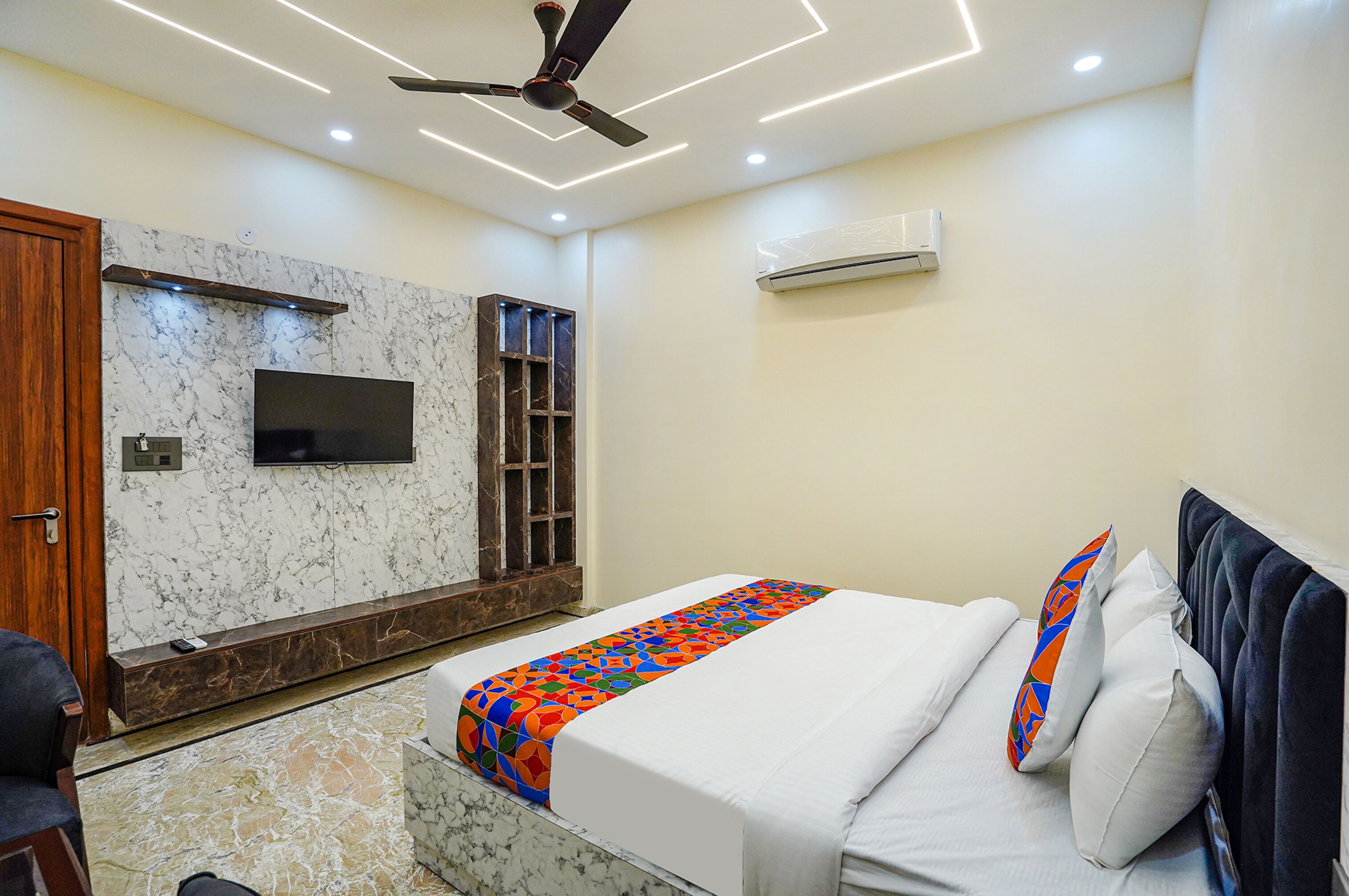A modern bedroom with a bed, a TV mounted on the wall, and a ceiling fan.
