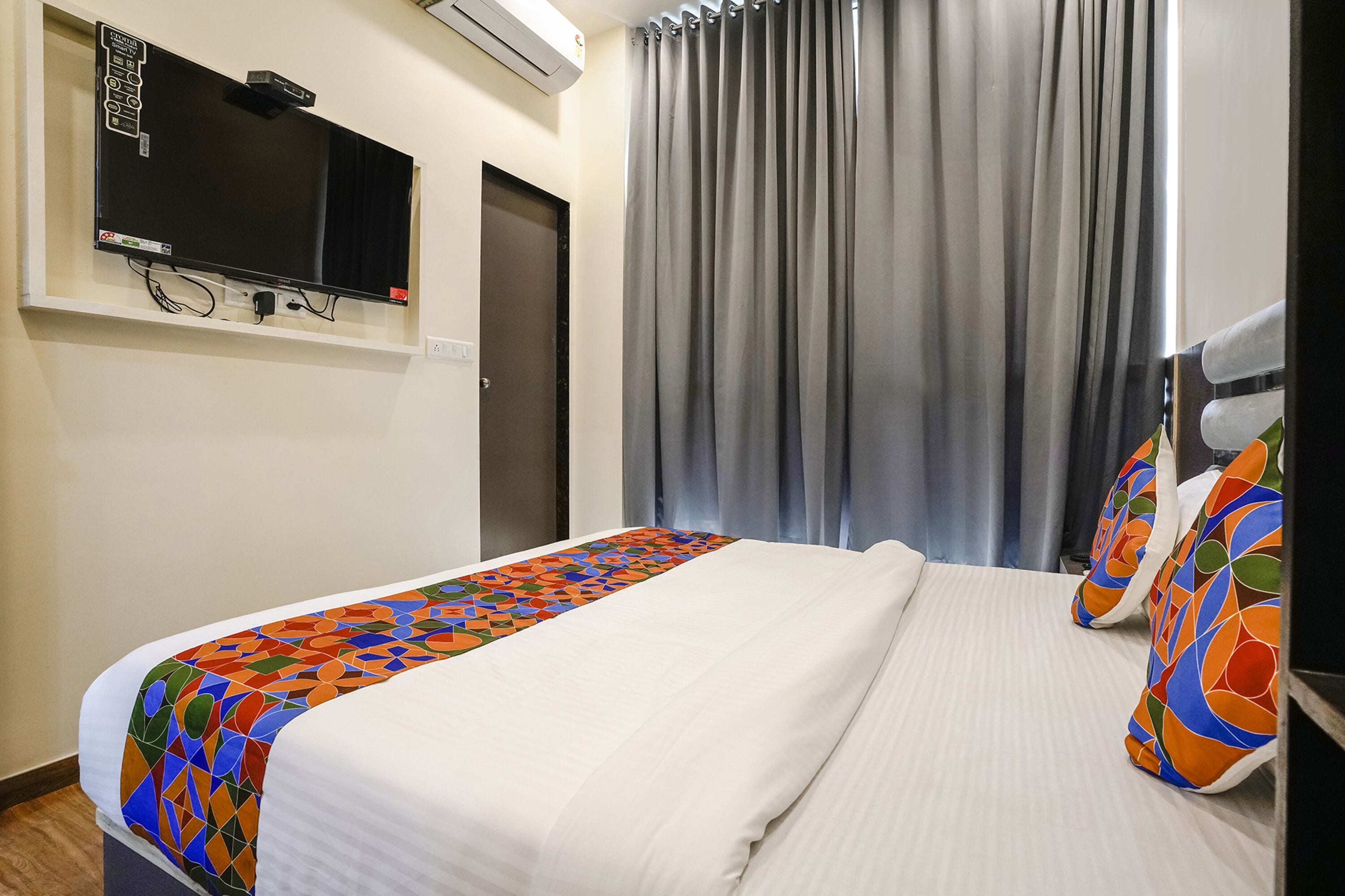 Ein Hotelzimmer mit einem Bett, einem an der Wand befestigten Fernseher und einem Fenster mit Vorhängen.