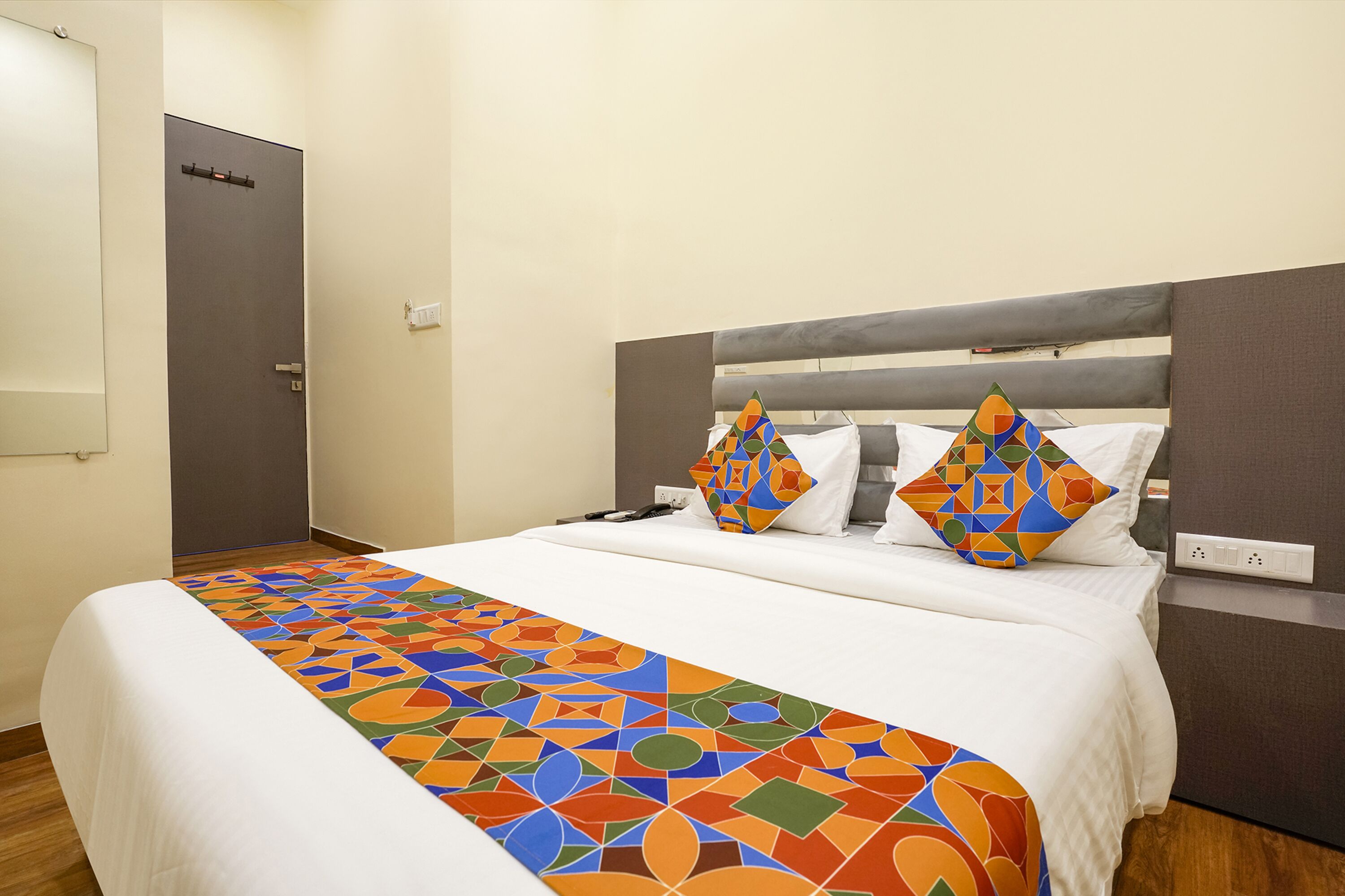 A hotel room with a bed, a patterned bedspread, and two geometric pillows.