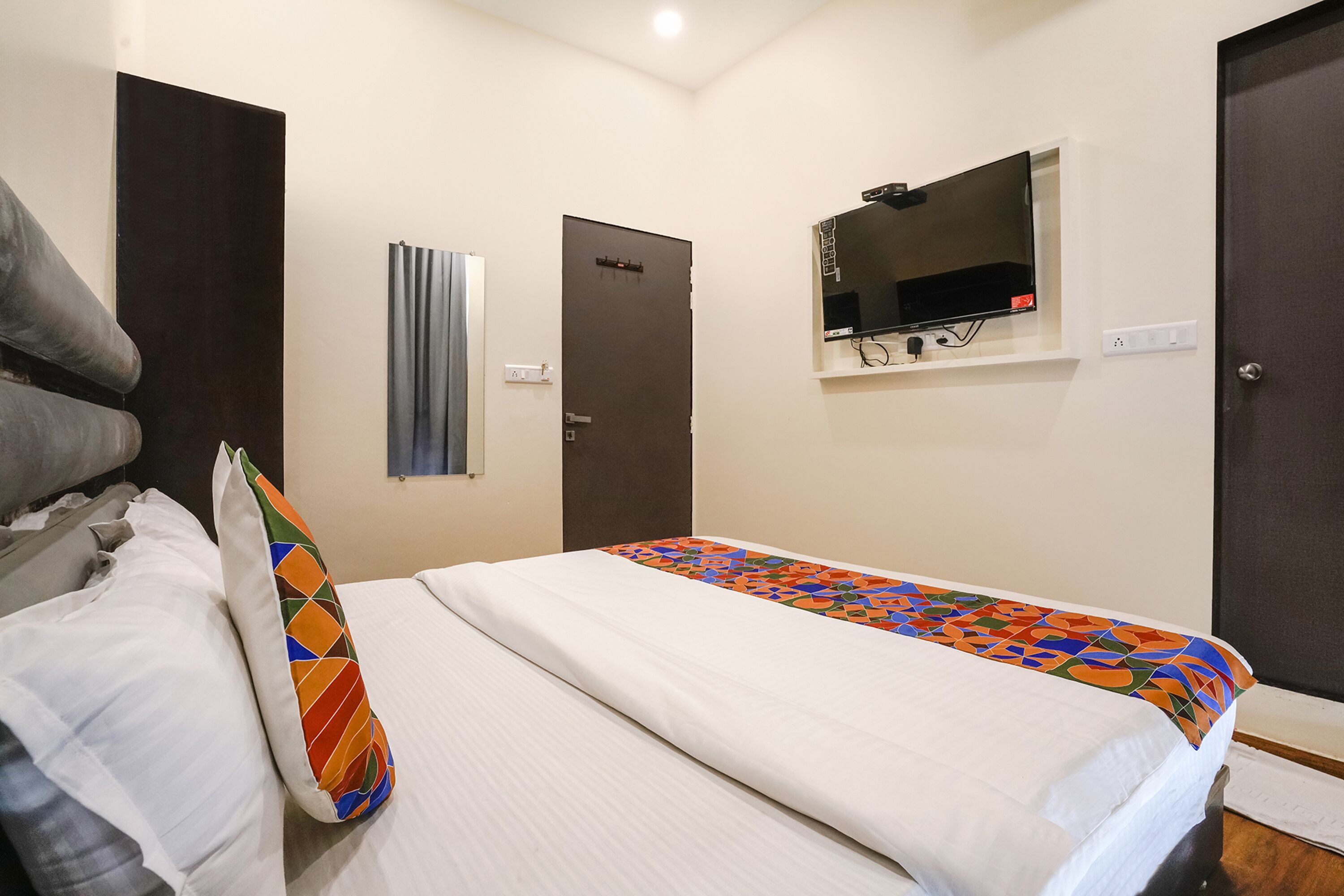A hotel room with a bed, a television mounted on the wall, and a door.