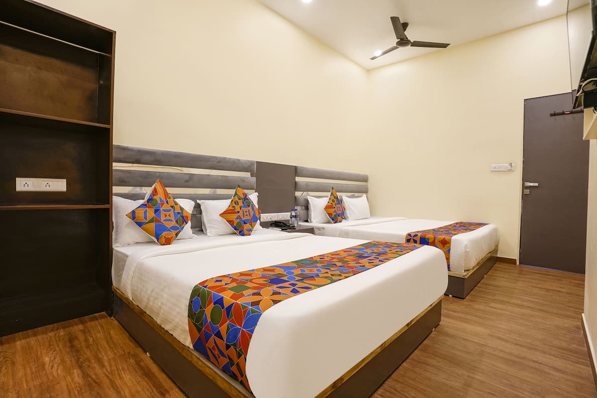 A hotel room with two beds, a wooden floor, a ceiling fan, and a wardrobe.