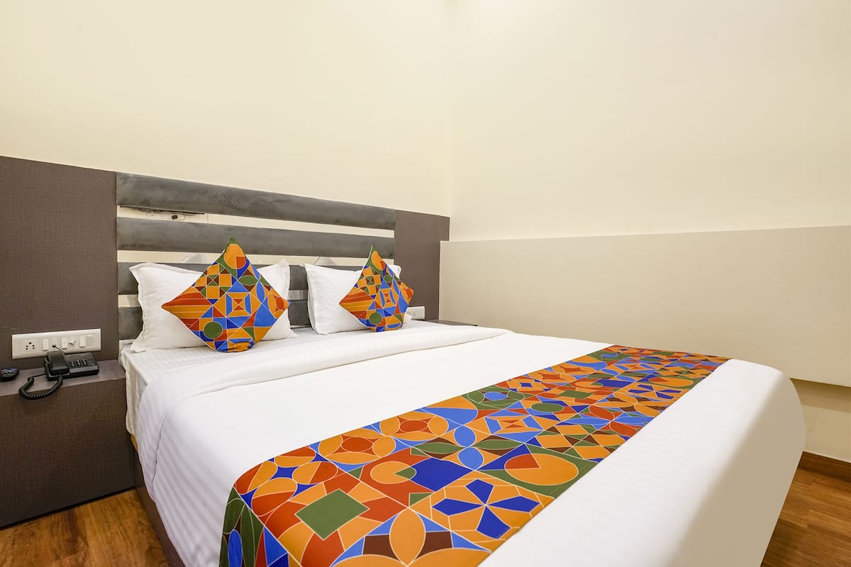 A neatly made bed with a patterned bedspread and two decorative pillows, a bedside telephone, and a power outlet on the nightstand.