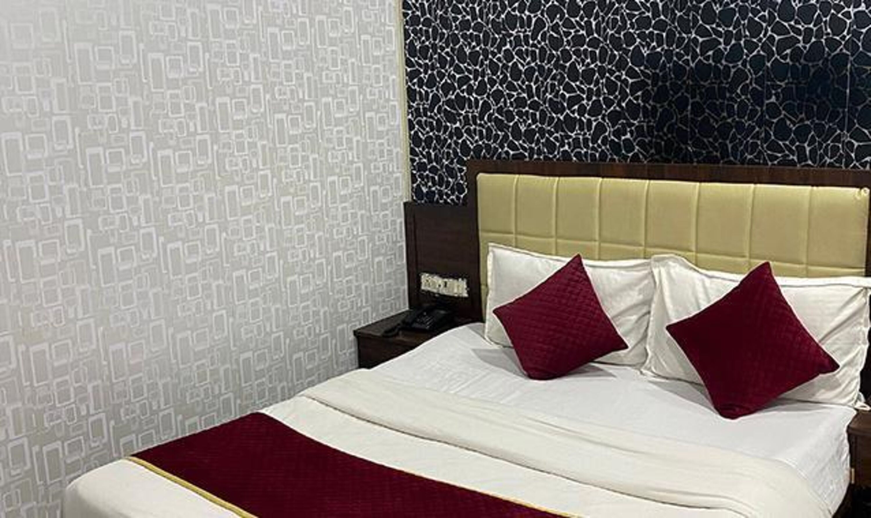 A hotel room with a bed, a nightstand, and a patterned wall.