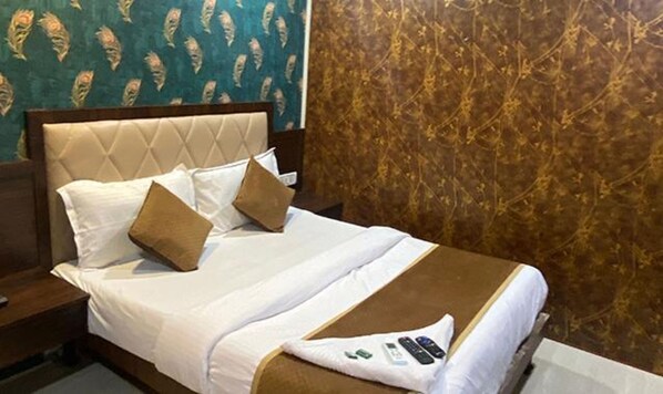 A hotel room with a bed, pillows, a blanket, and a remote control on the bed. - Fabexpress Ashirwad Residency (Mumbai)
