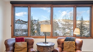Una habitación con dos sillones de cuero, una pequeña mesa de madera y vistas a un paisaje nevado a través de amplios ventanales.