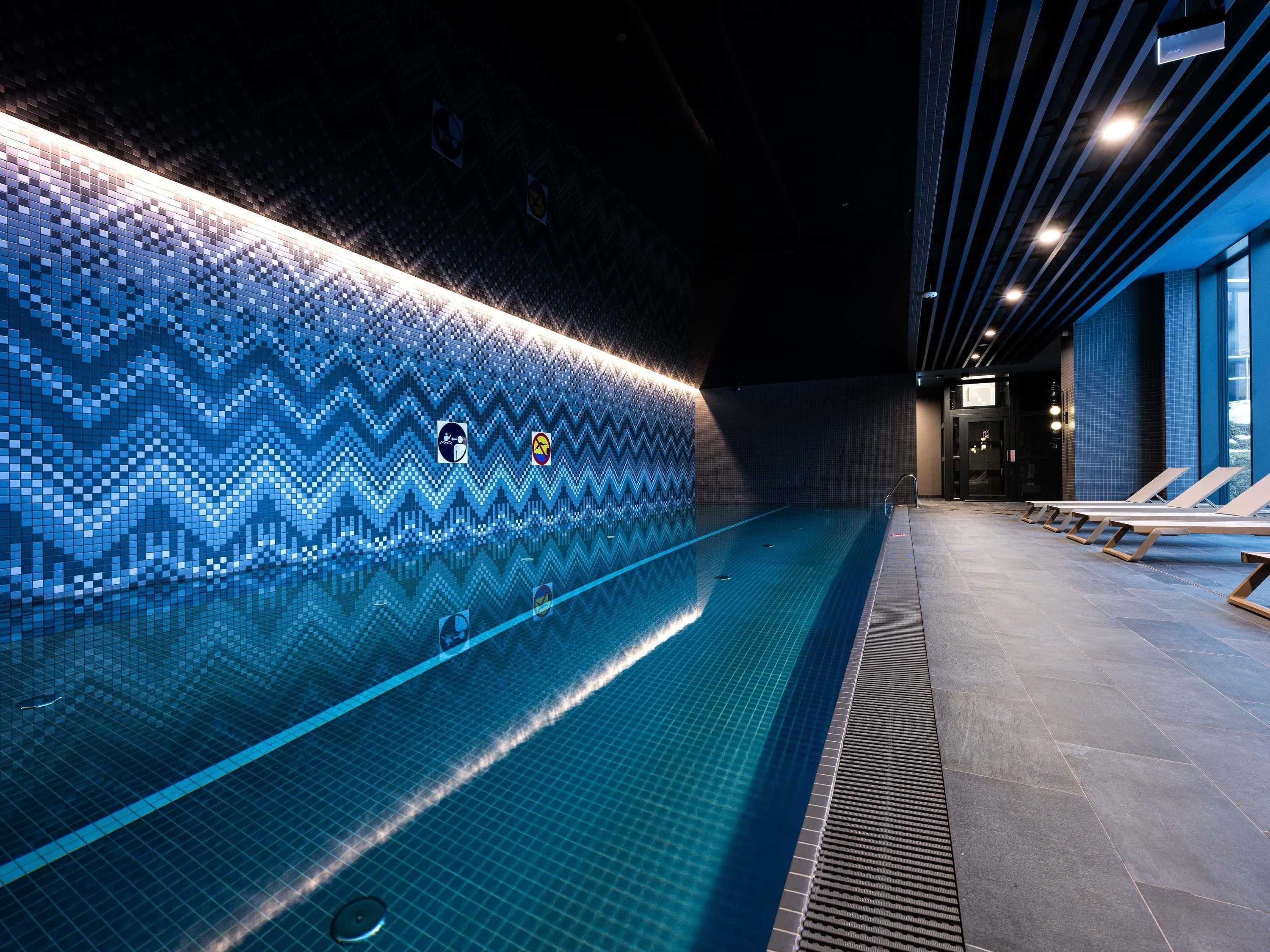 Ein Schwimmbecken mit Zickzack-Fliesenmuster, Liegestühlen und einer bepflasterten Wand mit Symbolen.