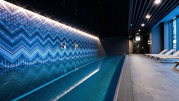 Ein Schwimmbecken mit Zickzack-Fliesenmuster, Liegestühlen und einer bepflasterten Wand mit Symbolen.