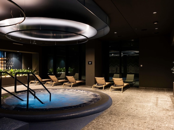 Een wellnessruimte met een whirlpool, lounge stoelen en een moderne plafondlamp.