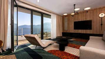 Une chambre d’hôtel moderne dotée d’une grande porte-fenêtre coulissante, d’un téléviseur à écran plat, d’un canapé, d’une table basse et d’un coin repas avec des chaises.