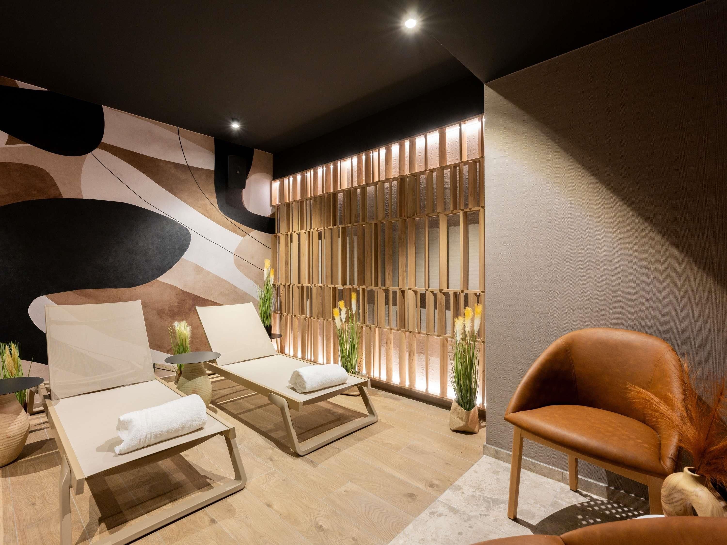 Ein moderner Wellnessraum mit zwei Liegestühlen, einer Holzwand und einem großen Fenster.