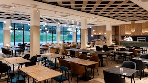 Un'ampia sala da pranzo con diversi tavoli e sedie, grandi finestre e un moderno design del soffitto.