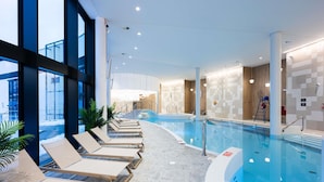 Une piscine intérieure moderne, dotée de chaises longues, d’un jacuzzi et offrant une vue sur l’extérieur.