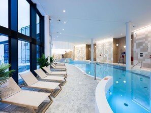Una piscina interior moderna con sillones de descanso, un jacuzzi y vistas al exterior.