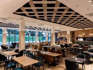 Un vaste espace dédié à la salle à manger, avec de nombreuses tables et chaises, de grandes fenêtres et un design moderne au niveau du plafond.