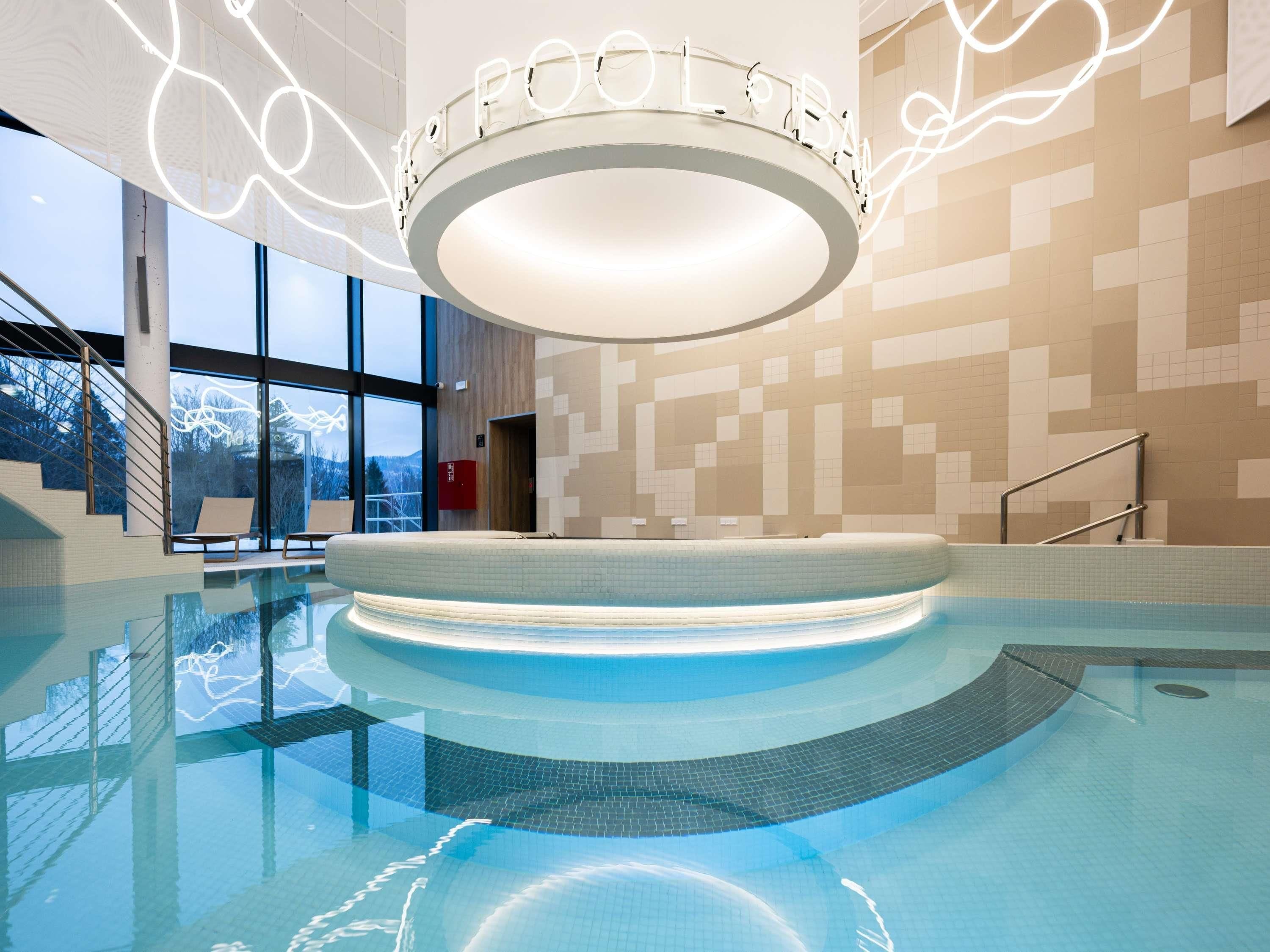 Ein moderner Innenpool mit einer runden Aussichtsplattform, großen Fenstern und einer geometrisch gefliesten Wand.