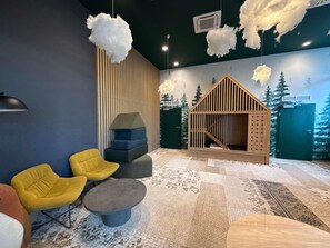 Une pièce au design moderne, comprenant une cabane en bois pour jouer, des chaises jaunes, une table ronde grise et un tapis à motifs.