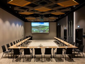 A conference room with a long table, black chairs, a projector screen displaying a landscape, and a modern ceiling design. - Mercure Szczyrk Resort (Szczyrk)
