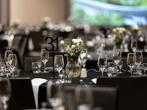 Uma mesa de banquete com lugares marcados por números, um vaso com flores e uma toalha de mesa preta.