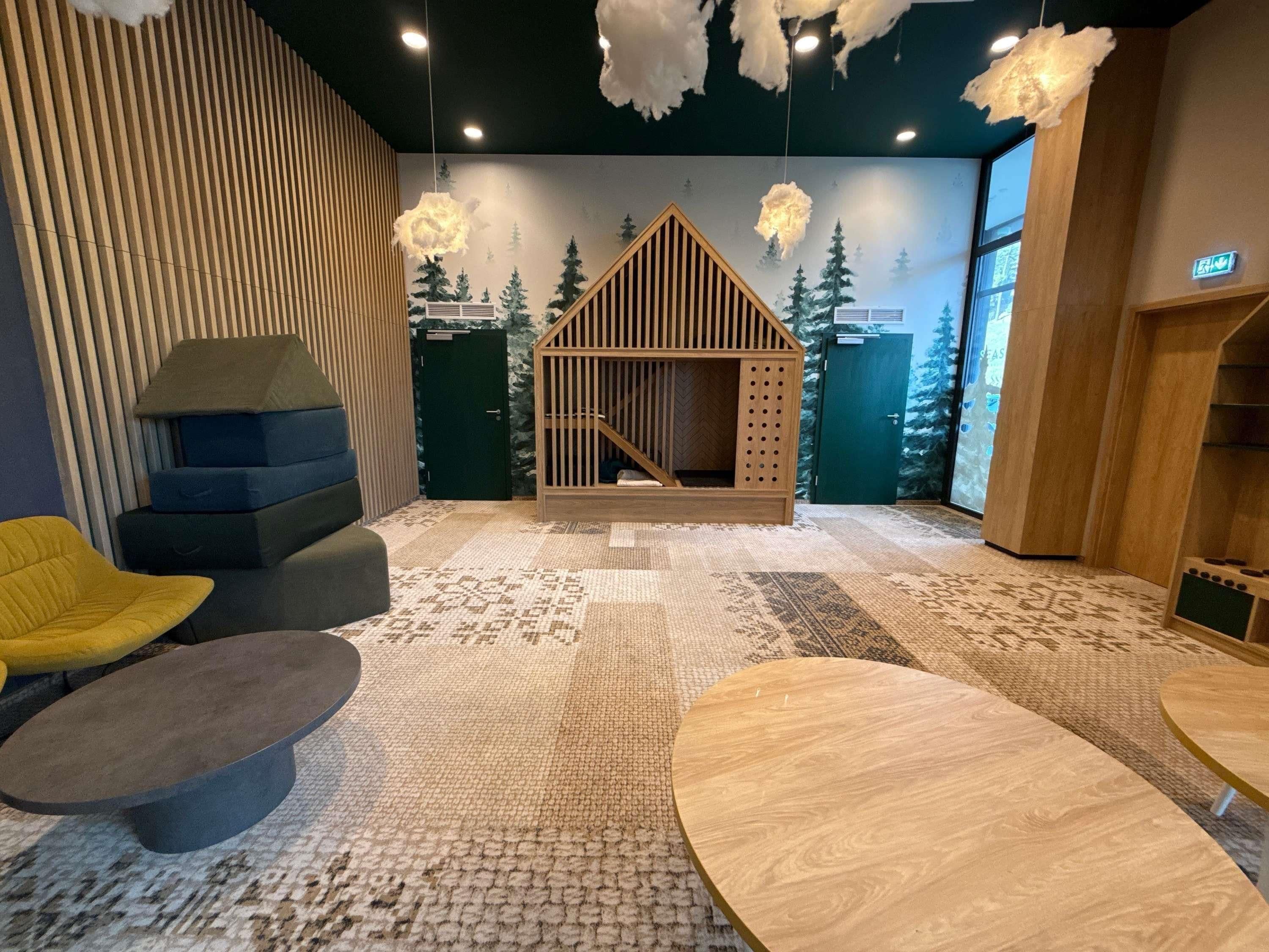 A cozy room with a wooden playhouse, a yellow chair, and a patterned carpet.