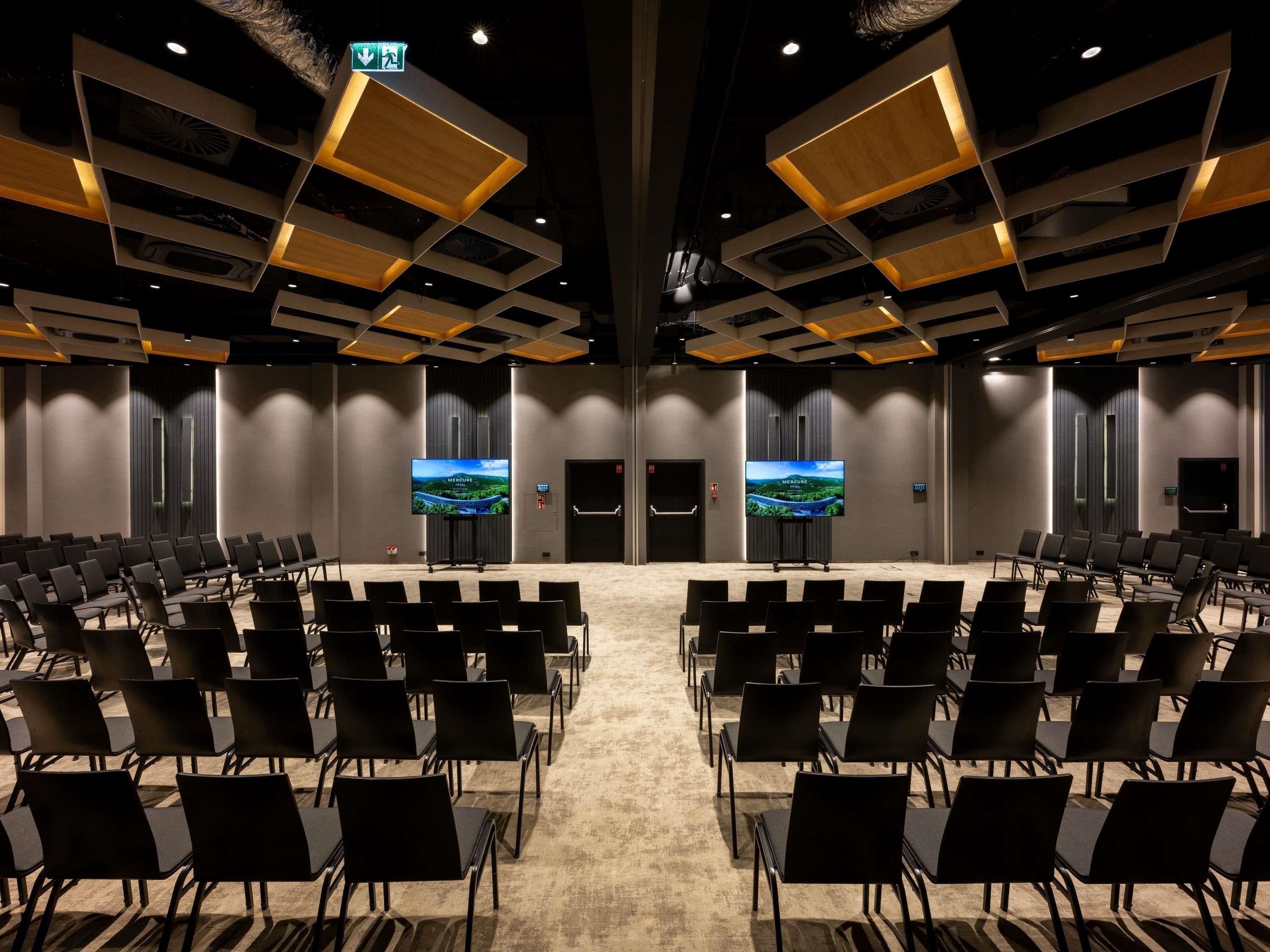 A conference room with rows of chairs, two large screens, and a modern ceiling design.